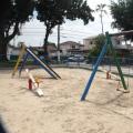 Play ground em praça, com conjunto de dois balancês, uma gangorra e um escorregador. #Paratodosverem