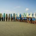 Surfistas estão na areia da praia. Eles posam para foto cada um com sua prancha oca em pé. #Pracegover