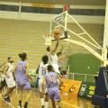 jogo de basquete. Um jogador salta com a bola em direção à cesta, bem próximo à ela. Outros jogadores estão em volta. #paratodosverem