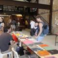 Livros expostos sobre uma bancada. Há um vendedor do lado esquerdo da foto. À direita, um homem olha as publicações