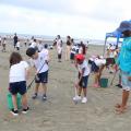 alunos uniformizados recolhem resíduos da areia da praia. #paratodosverem