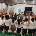 alunos estão de mãos dadas para o alto, reunidos em roda. #paratodosverem 