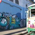 grafite em muro com bonde passando ao lado. #paratodosverem
