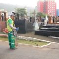 homem uniformizado capina canteiro e outros dois lavam chão. #paratodosverem