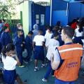 Crianças e pessoal de apoio da Defesa Civil nas dependências da escola. #Pracegover