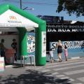 movimento de rua com mãe passeando com dois filhos, à esquerda uma tenda verde e branca
