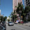 imagem da avenida com carros, motos estacionadas e prédios ao fundo #paratodosverem