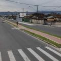 Trecho de avenida pavimentado, com faixa de pedestre e ciclovia no centro. #Pracegover