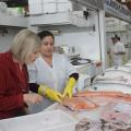 Cliente observa salmão exibido por profissional paramentada com luvas. #paratodosverem