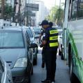 guardas municipais estão em pista de avenida, com carros parados. Eles estão entre carros e ônibus distribuindo folhetos. #paratodosverem