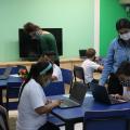 crianças mexem no computador e professoras orientam #paratodosverem