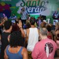 Público, de costas, assiste apresentação de cantor no palco com banner Santos Verão. #pracegover