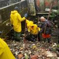 operários vestindo capas de chuva removem manualmente lixo de canal. #paratodosverem