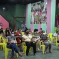 Mulheres sentadas observam instrutora em palestra na quadra da escola de samba União Imperial. #pratodosverem