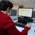 Mulher, com roupa vermelha, trabalha olhando para tela do computador. #pracegover