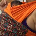 Mulher de máscara usando sling na cor laranja, com recém-nascido junto ao corpo. #pracegover