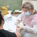 mulher faz teste de HIV/sífilis em homem que está de costas para a foto. O exame é feito com a retirada de uma gota de sangue do dedo. #paratodosverem
