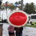 duas mulheres estão sob guarda-chuva que está envergado devido ao vento. #paratodosverem