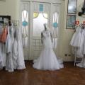 vestidos de noiva e de damas de honra estão pendurados em duas araras. Ao centro, um vestido em um manequim. #paratodosverem
