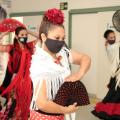 close de mulher dançando flamenco, com roupa típica, o que inclui xale nos ombros, saia rodada e flor na cabeça, além de um leque aberto nas mãos. Atrás há outras mulheres também dançando. #paratodosverem
