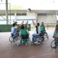 Seis jovens em cadeira de rodas erguem as mãos em disputa de bola de basquete dentro de quadra