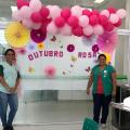 Funcionárias de policlínica estão diante de um painel com balões de gás cor de rosa. Ao fundo se lê Outubro Rosa. #Pracegover