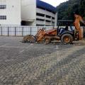 Trator remove piso remanescente de área descoberta. Ao fundo se vê o prédio da Arena Santos. #Pracegover