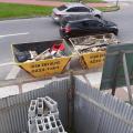 Tijolos vazados para obra em primeiro plano. Ao fundo, do lado de fora da construção, há duas caçambas com material depositado. #Pracegover