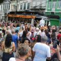 #pracegover Cerca de 300 pessoas observam bonde decoração de carnaval chegando à praça