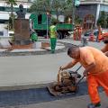 trabalhadores usando máquina para cimentar piso junto a uma praça #paratodosverem