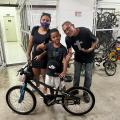 mãe e pai ao lado de filho que segura a bicicleta #paratodosverem