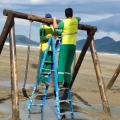 homens instalam equipamento na praia #paratodosverem
