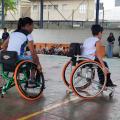 mulher e criança estão em cadeiras de rodas em quadra esportiva. #paratodosverem