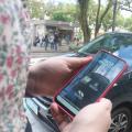 Mulher segura celular com aplicativo do Zona Azul e carro ao fundo. #pratodosverem