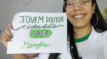 jovem mostra cartaz que diz jovem doutor cidadão para sempre #paratodosverem