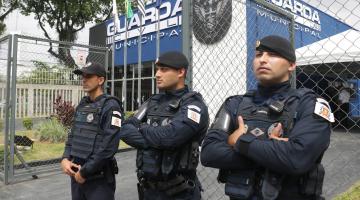 três guardas municipais parados diante de prédio da corporação onde se lê guarda municipal na fachada. #paratodosverem 