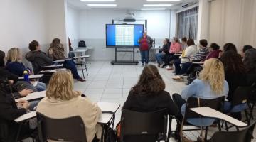 pessoas reunidas em sala de aula sentadas em cadeiras dispostas em formato de roda. Há um telão no fundo. #paratodosverem