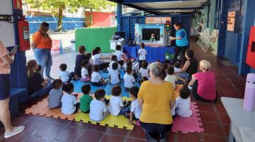 crianças estão sentadas no chão assistindo a apresentação de fantoches. #paratodosverem