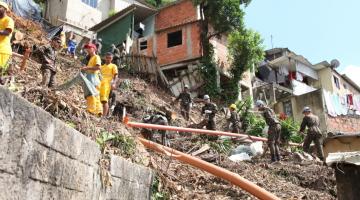 Equipes da Terracom e soldados do Exército no alto de uma encosta fazendo limpeza. #Paratodosverem