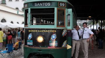 bonde das nações está parado na estação. várias pessoas estão em volta. #paratodosverem