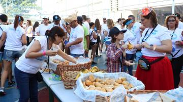 No pátio da escola, mesa posta com pães é rodeada por voluntários do projeto uniformamizados de camiseta branca
