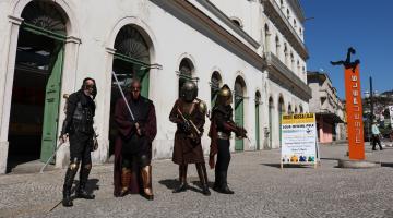 Quatro pessoas vestidas de personagens futurísticos, com capacetes e espadas, posem à frente do Museu Pelé
