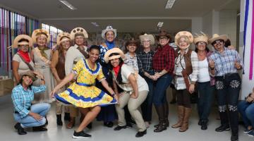 Quatorze mulheres com trajes de festa junino, femininos e masculinos, posam para foto