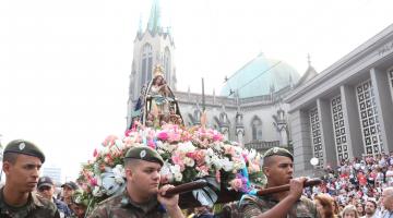 Soldados carregam a santa em andor. Eles passam na frente da Catedral e do fórum. 