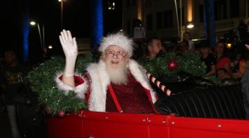 Idoso vestido de papai noel acena ao público em banco traseiro de carro