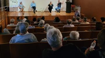 publico está sentado em auditório assistindo palestra. #paratodosverem