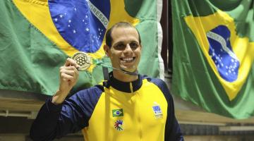 atleta exibe medalha com bandeira do brasil ao fundo #paratodosverem