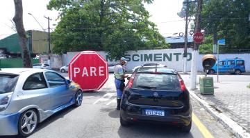 agente da CET na rua está abordando motorista que está dentro de carro. Ao fundo, um grande inflável onde se lê Pare. #paratodosverem