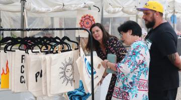 pessoas olham produtos em barraca #paratodosverem