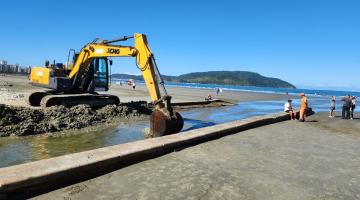 escavadeira está na beira do canal na praia recolhendo areia acumulada. #paratodosverem